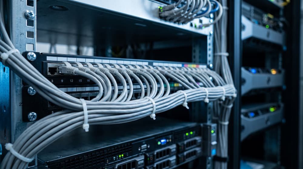 Panel de parcheo en un armario rack con decenas de cables Ethernet grises ordenados.